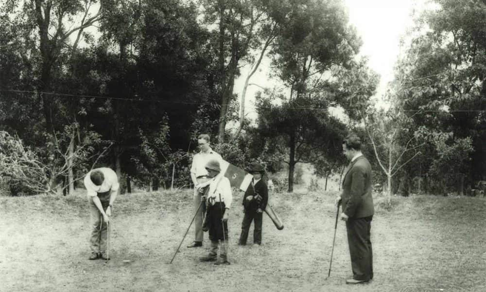 Fűben fekvő felesége csücsöri ajkaira helyezte a labdát a golfjátékos